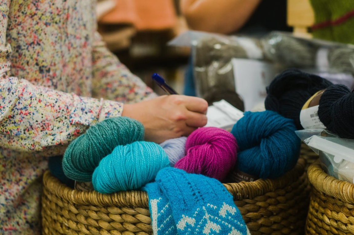 Kvinne noterer på strikkeoppskrift over fire garnnøster og strikketøy i fine farger.